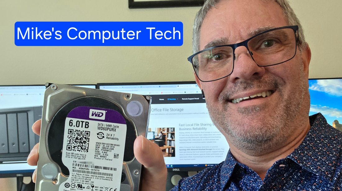 Michael Challis holding a Western Digital hard drive in front of a computer monitor displaying Mike's Computer Tech website.